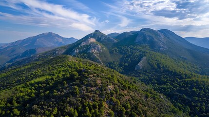 Fototapeta premium Aerial view of lush green mountains under a blue sky with wispy clouds, showcasing natural beauty and tranquility.