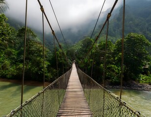 Obraz premium Swinging bridge over a tropical river surrounded by misty mountains and dense jungle