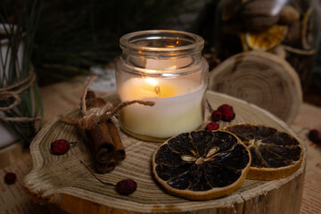 Cozy scene of a vanilla candle cinnamon sticks and dried oranges on a wood platform with Christmas background