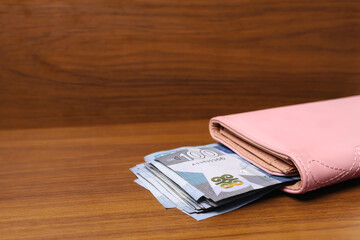 100 Ghanaian cedi money currency notes inside a pink purse on brown wooden background with copy space