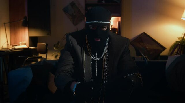 Zoom in portrait of Caucasian young male robber in balaclava posing for camera with necklaces holding crowbar