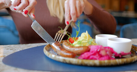 Woman Cutting Sausage with Sides of Mashed Potatoes and Vegetables