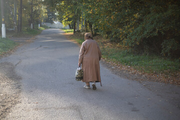 Pensioner walking on the road. Elderly woman with a walking stick.