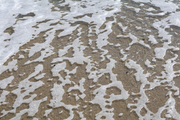 Obraz premium Close-up of intricate sea foam patterns on a sandy beach, showcasing the beauty of ocean textures.