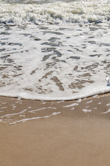 Close-up of soft sea foam spreading over wet sand, highlighting the serene beauty of a coastal shoreline.