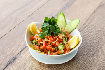 Fresh Vegetable Salad including green chilli, cabbage, tomatoes, cucumbers, lemon and coriander served in a white bowl isolated on wooden table side view of arabic salad