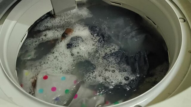 Dirty clothes spinning in a top-loading washing machine. Laundry and house keeping concept