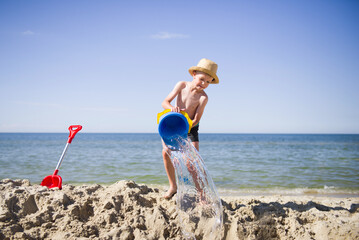 Happy little boy pouring water from plastic bucket on the sea beach during vacation © Piotrek