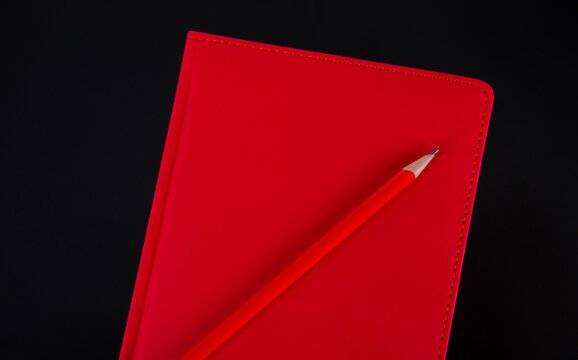 red notebook and pencil on black background