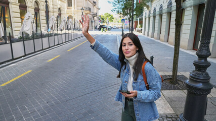 A woman walks quickly, looking at the street and stopping a taxi. The bustling city life is all around her.