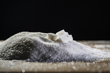 Sugar cubes on a pile of white refined granulated sugar, close up. Weight gain and risk of heart disease concepts.