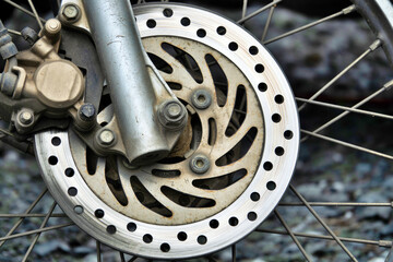 A close up of a motorcycle's rear wheel with a large, rusted, and worn out brake disc