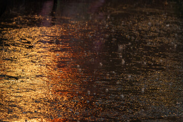 A wet street with raindrops on the ground. The water appears to be reflecting the light, creating a beautiful and serene atmosphere