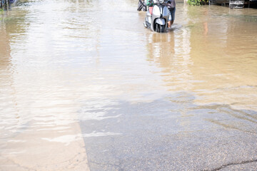 Obraz premium A flooded street with a man on a scooter. The water is murky and the street is covered in mud