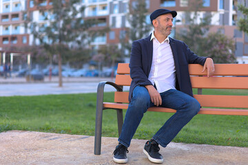 Obraz premium Man sitting on a bench in the park calm and thoughtful looking into the distance