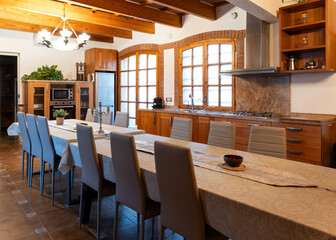 Rustic kitchen and dining area featuring a large table, wooden beams, tile floor, and wooden cabinets
