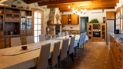 Large dining room table with modern chairs in a rustic home featuring a stone fireplace, wooden beams, and an open kitchen
