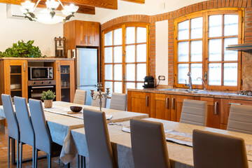 Rustic kitchen with wooden furniture, brick walls, and large windows, featuring a spacious dining table and chairs
