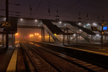 Deserted platforms of a railway station. Orange lanterns in the fog are reflected on the wet...
