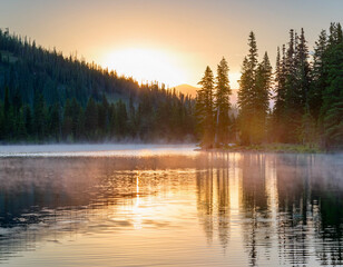 Fototapeta premium Sunrise over a tranquil mountain lake mist rising from the water