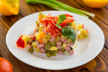 vegetable salad of boiled vegetables, with peas, sausage, sweet pepper. On a wooden table