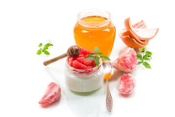 homemade sweet yogurt in a glass jar with pieces of red ripe grapefruit and honey, isolated on white background