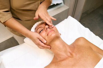 Middle aged woman enjoys hand anti-aging facial treatment in spa salon.