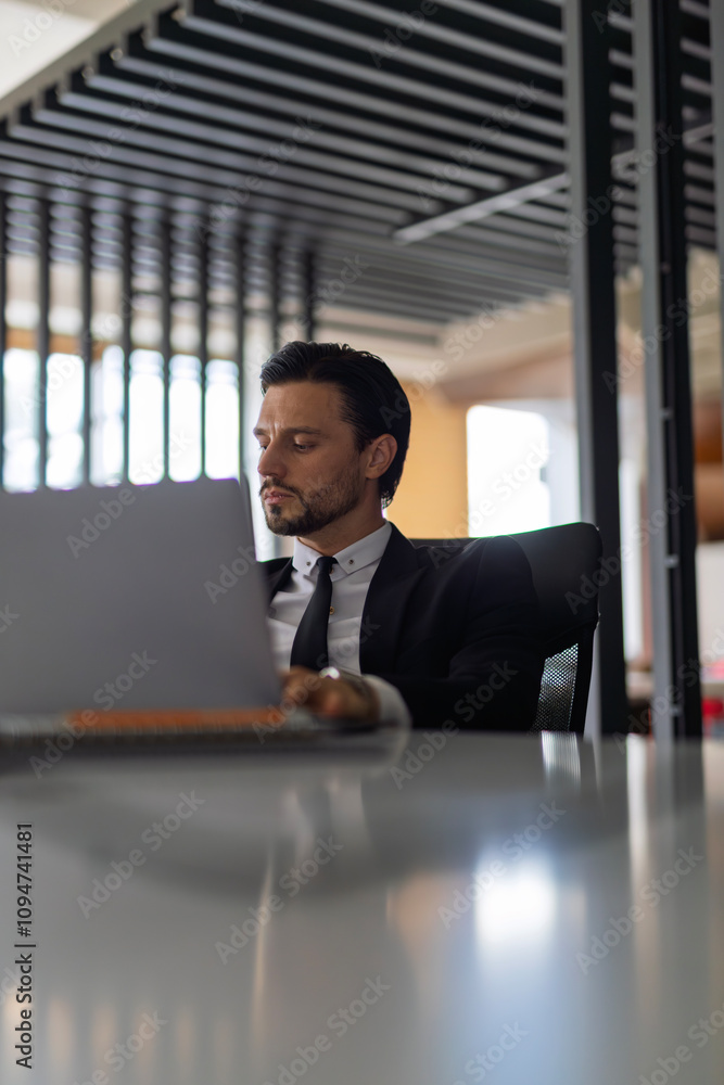Poster a man in a suit is sitting at a desk with a laptop open in front of him. he is focused on his work, 