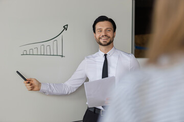 A man is standing in front of a white board with a graph on it. He is smiling and holding a marker....