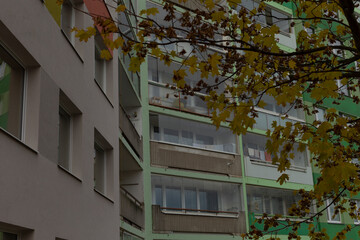 A tall apartment building featuring numerous balconies set against a vibrant background of leafy trees