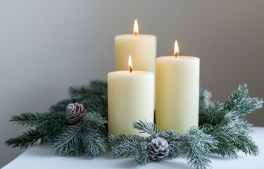 Three lit candles with frosted pine branches and pinecones