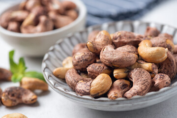 Unpeeled dry cashew nuts on a plate, closeup view