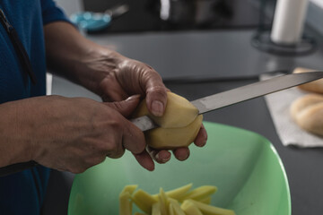 Woman's hands cut and peel potatoes for French fries