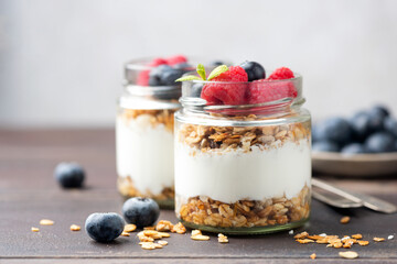 Greek yogurt parfait with granola and fresh berries in a jar on grey background. Healthy vegetarian...
