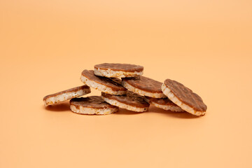 Stack of chocolate covered rice wafers on an orange background. The waffles are stacked on top of each other. The concept of indulgence and satisfaction as the waffles are piled high and seem deliciou