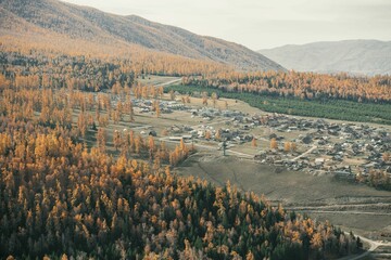 Aerial view of rural village amidst autumnal forests.