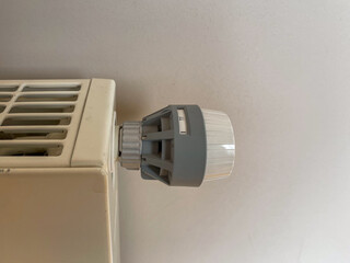 A white radiator with a grey thermostat on it. The thermostat has a white and grey color