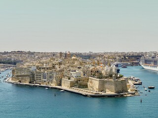 Fototapeta premium Aerial view of Senglea's historic fortified city, surrounded by the blue waters of the Grand Harbour, with ships and yachts nearby.