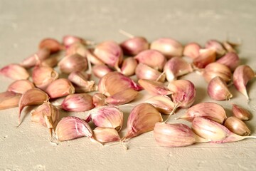 A pile of fresh garlic cloves spread out on a light textured surface, highlighting their natural color and detail.