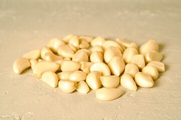 A pile of peeled garlic cloves spread out on a light textured surface, highlighting their smooth texture and natural color.