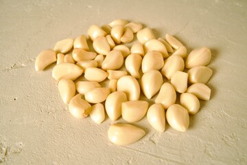 A pile of peeled garlic cloves spread out on a light textured surface, highlighting their smooth texture and natural color.