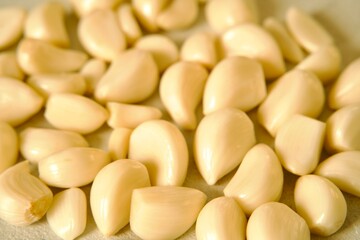 A pile of peeled garlic cloves spread out on a light textured surface, highlighting their smooth texture and natural color.