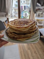 A hand holds a plate filled with a generous pile of freshly baked khachapuri. The golden, flaky crust glistens, revealing hints of the warm, gooey cheese filling inside. 