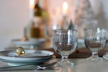 Table set for Christmas meal with plates, glasses, holiday decorations, lit candles and wine. Selective focus.