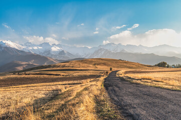 Old road among autumn dry meadows and hills. Autumn in the mountains in Kyrgyzstan.