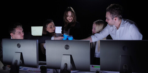 Men and women leaders team work at desks with monitors in dark office, yearend corporate meeting,...