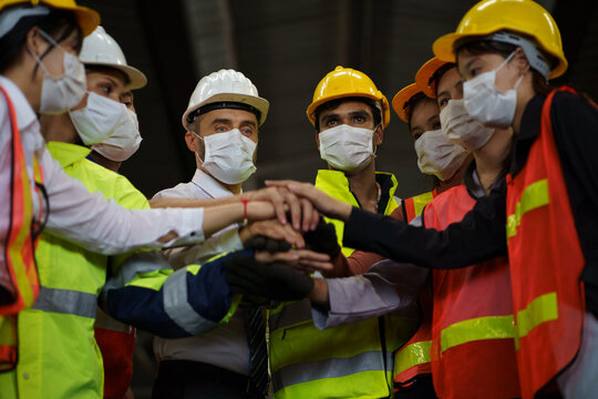 group of industry Engineer and worker factory wearing protective face mask stacking their hands or joining hands together in manufacturing