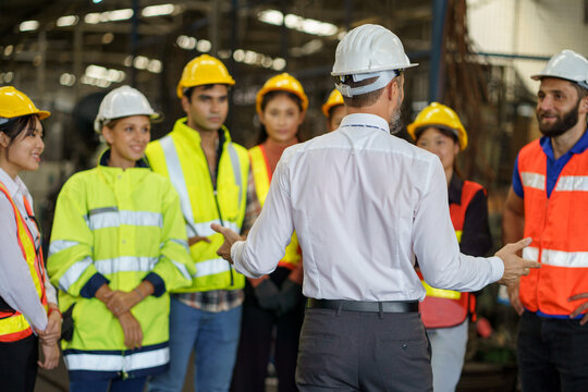 group of diversity engineer factory worker standing in morning meeting with business man manager or executive boss leader team talking and brief in industry manufacturing warehouse. back or rear view