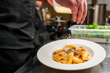 A chef sprinkles grated cheese over a plated dish of rigatoni pasta, showcasing a delicious...