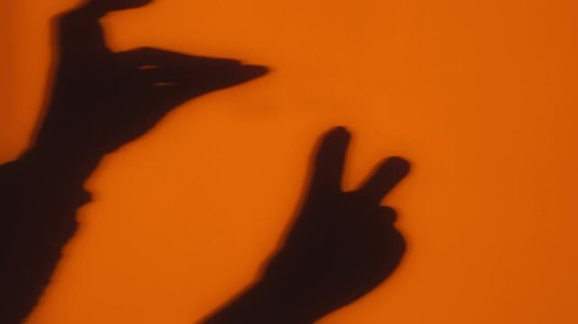A creative display of hand shadows forming puppet shapes against a warm orange backdrop, evoking a sense of playfulness and imagination.